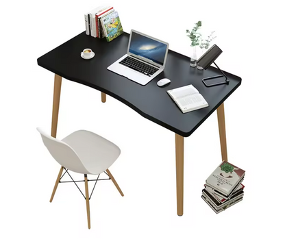 A simple design computer desk with a black rectangular MDF top and wooden legs, displayed in a home setting with a laptop, books, and a plant on it.